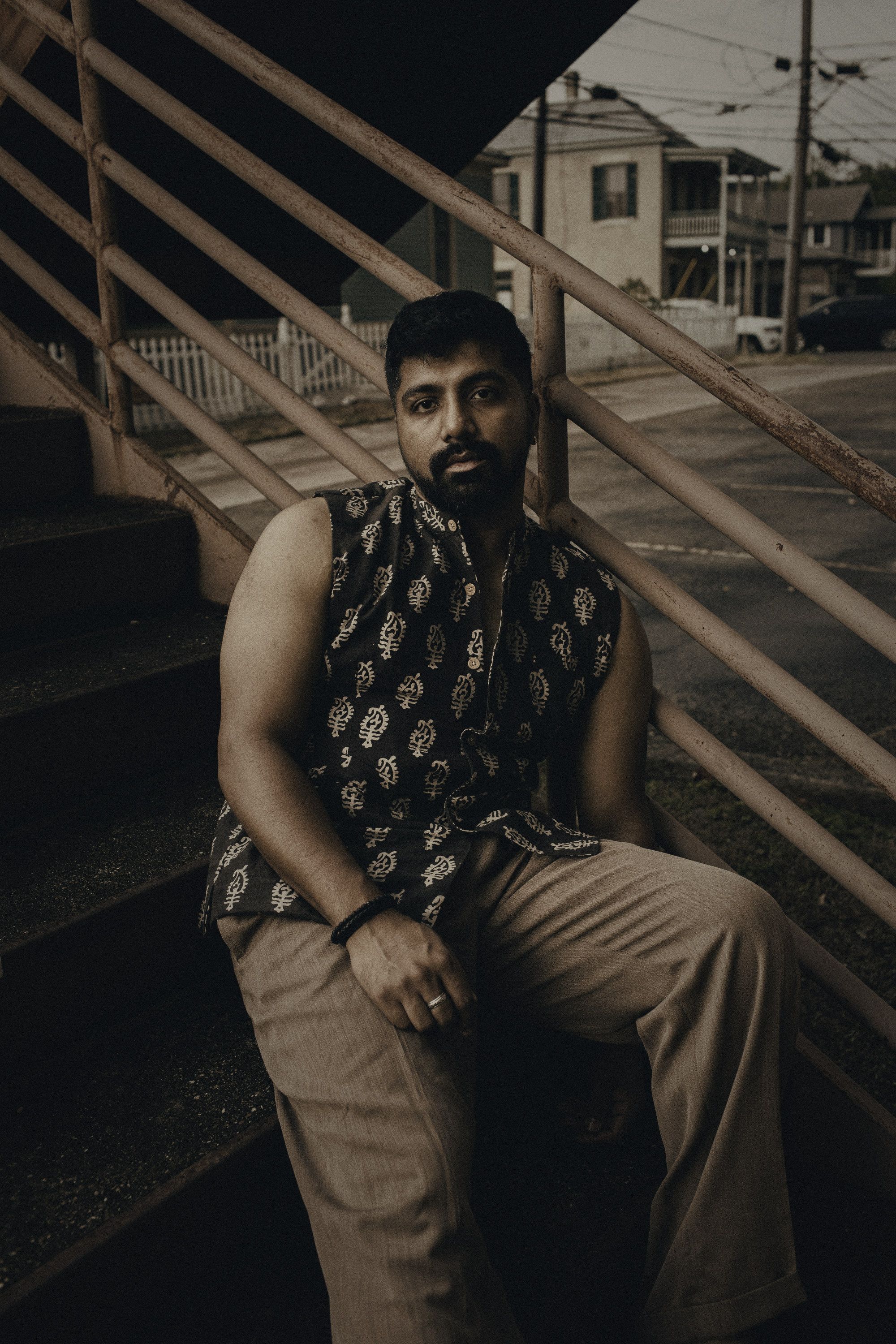 Adi Rao seated on a rusted exterior stairwell at dusk, in a printed vest.
